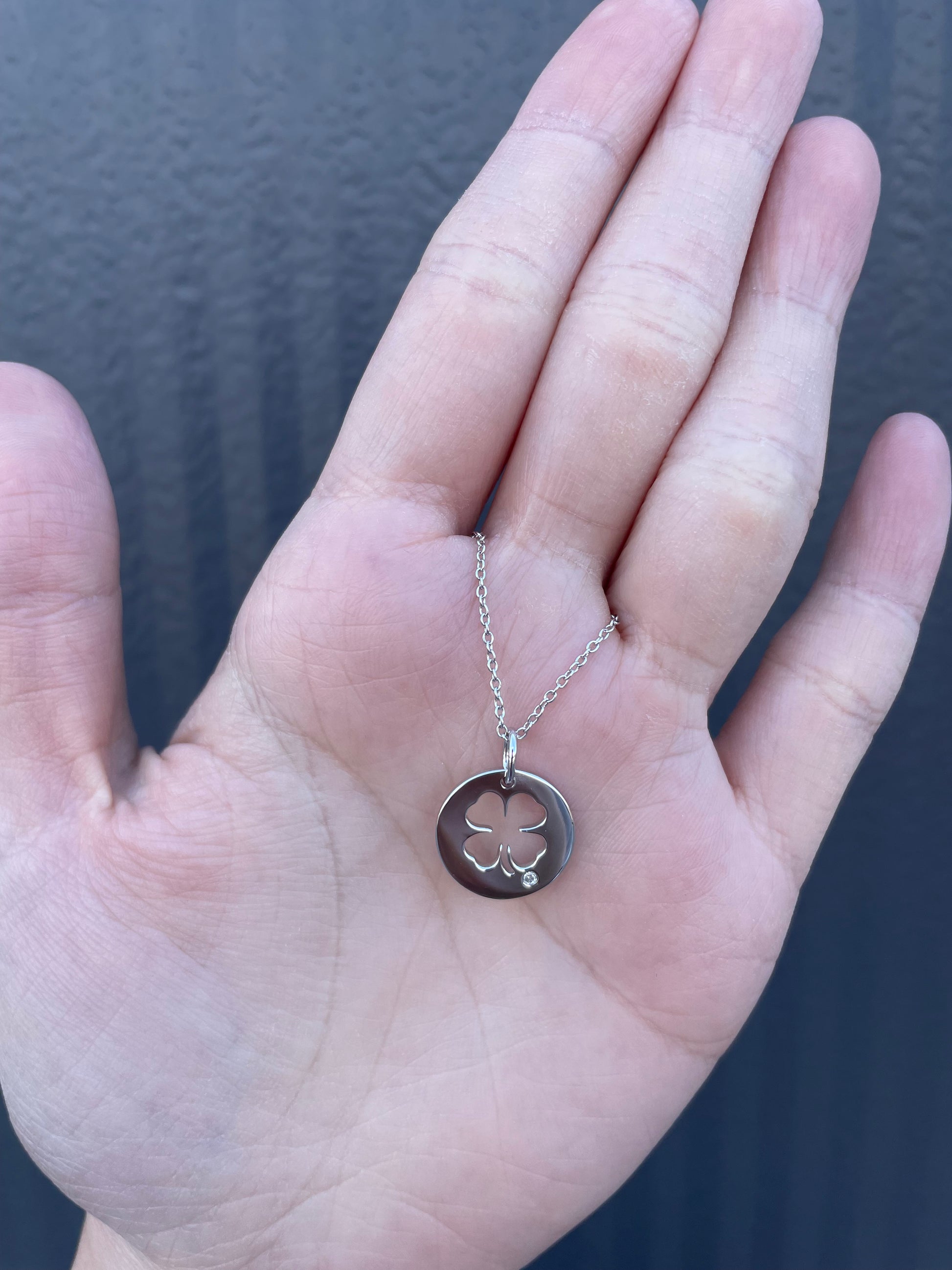 Hand holding a 925 sterling silver four-leaf clover outline pendant necklace with a genuine Canadian diamond accent, featuring a delicate rolo chain.