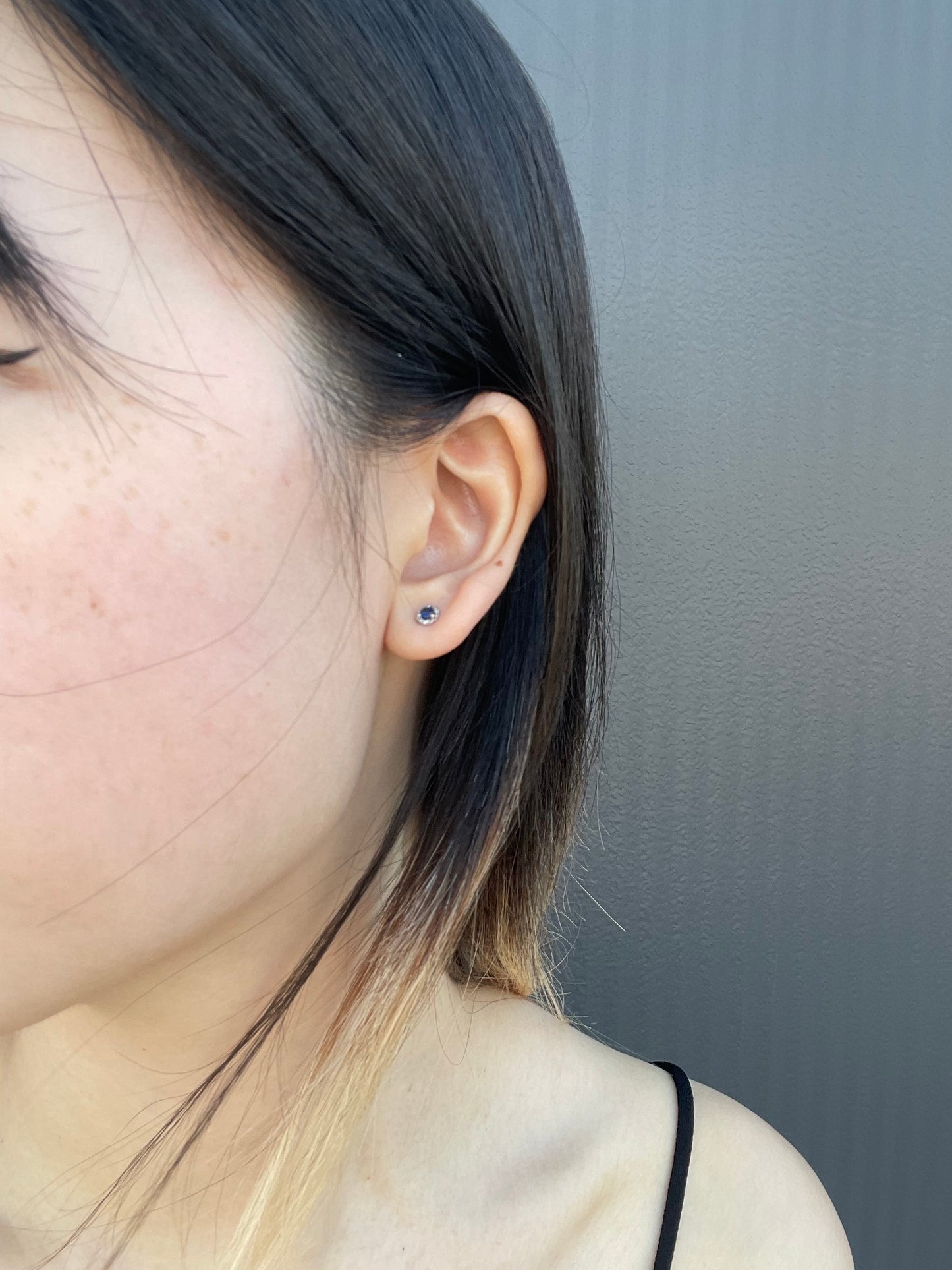 Close-up model photo showcasing a 925 sterling silver halo stud earring, featuring a round 1/3 Cttw blue sapphire center stone closely surrounded by a sparkling 1/10 Cttw diamond halo frame.