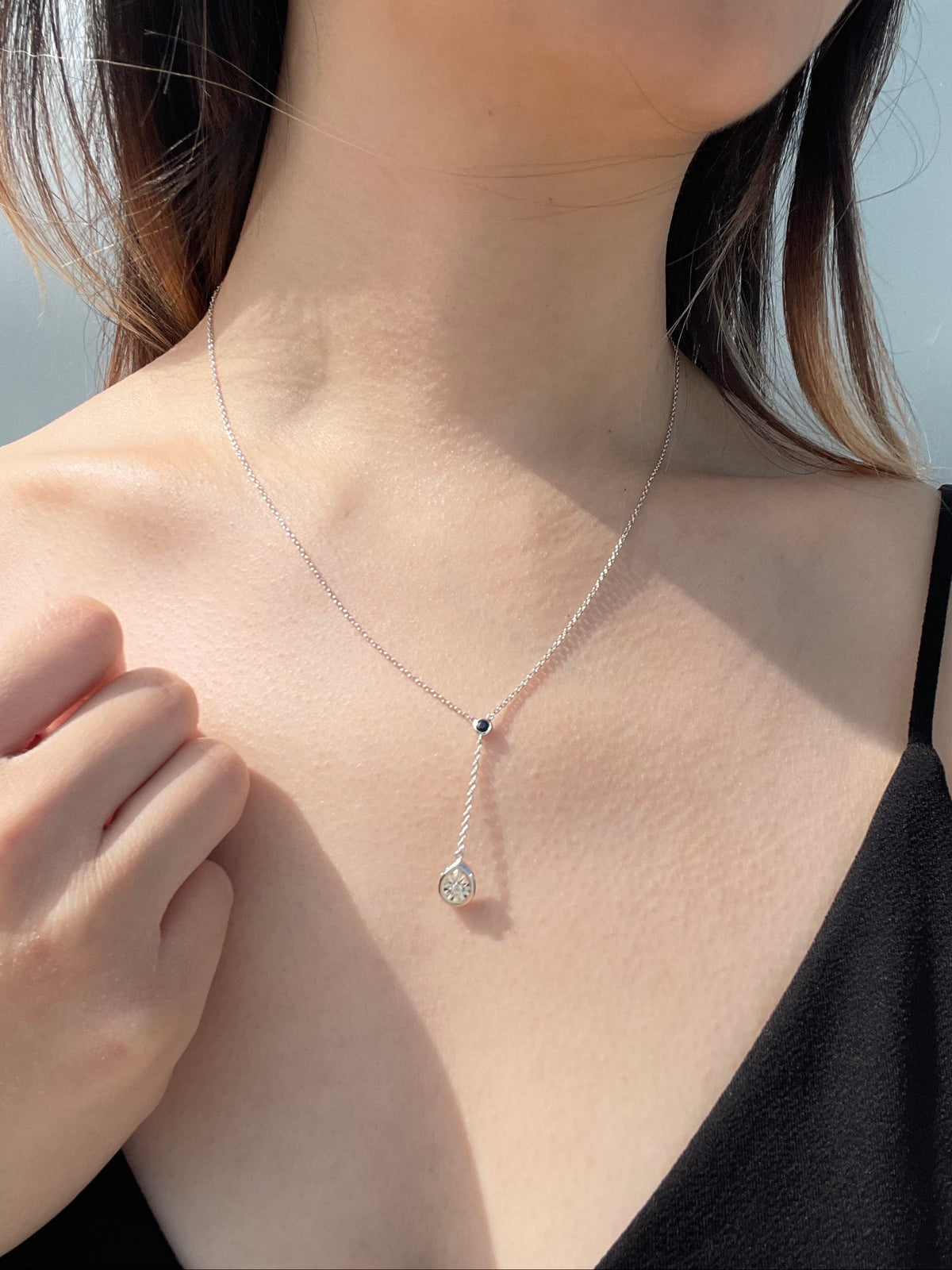 Close-up model photo showcasing a sterling silver Y-style necklace, featuring a small round blue sapphire accent at the junction and a dangling pear-shaped pendant with a miracle-set white diamond.