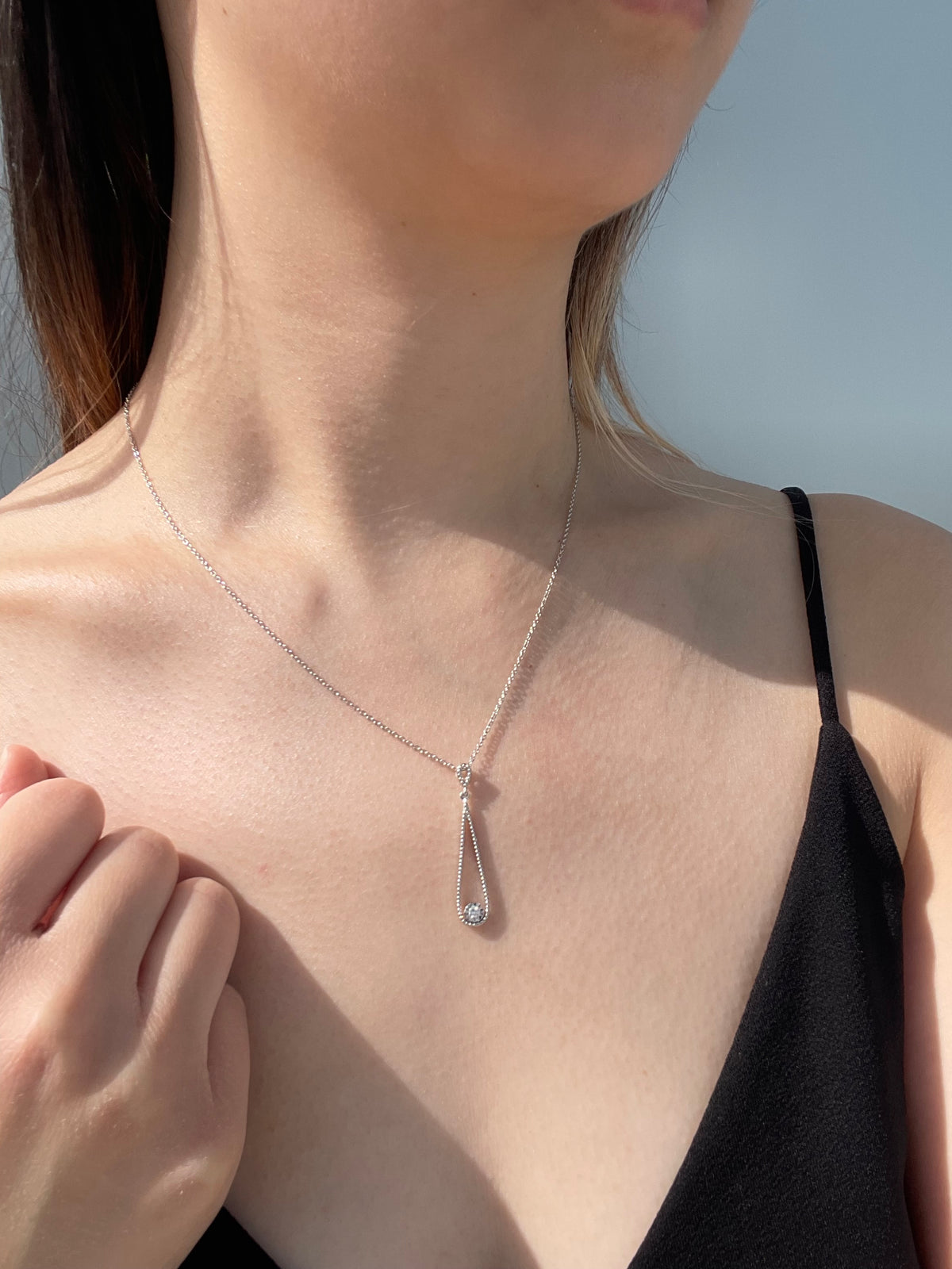 Close-up model photo showcasing a 925 sterling silver open teardrop pendant necklace on a neckline, highlighting the elegant drape and the way the delicate milgrain texture frame and 0.06 Ct solitaire Canadian diamond  catch the light.