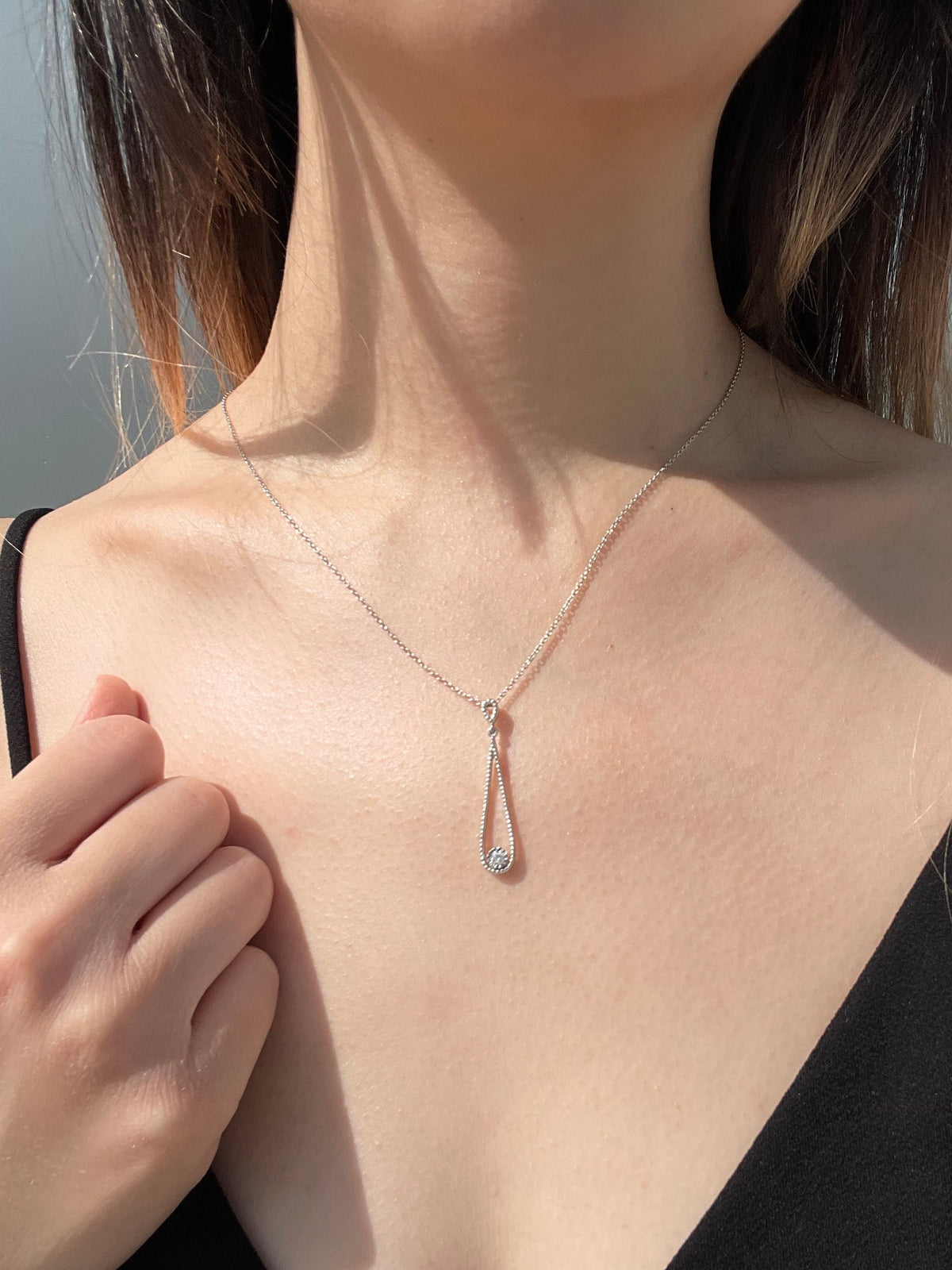 Close-up model photo showcasing a 925 sterling silver open teardrop pendant necklace on a neckline, highlighting the elegant drape and the way the delicate milgrain texture frame and 0.06 Ct solitaire Canadian diamond  catch the light.