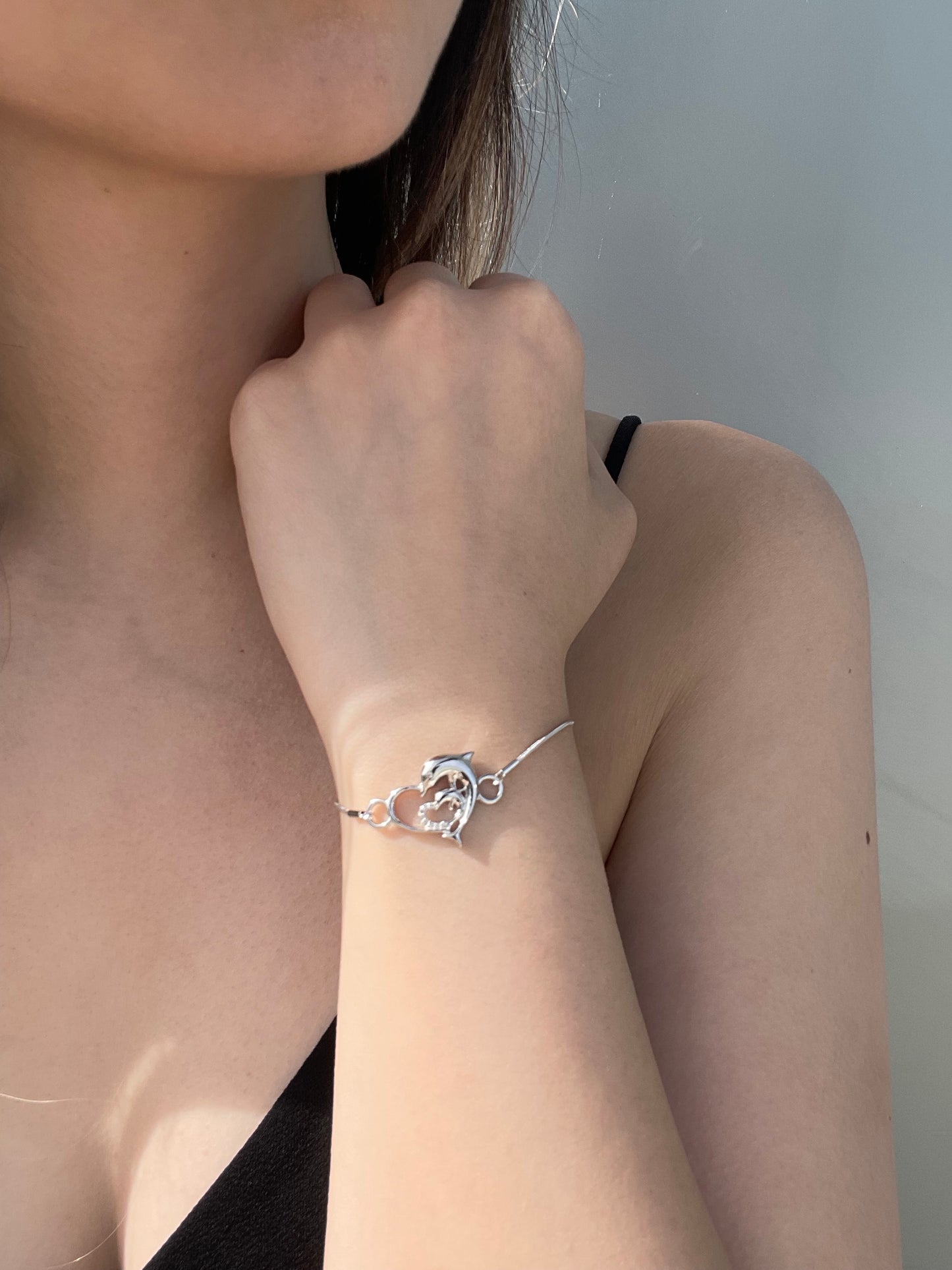 Close-up model photo showcasing a 925 sterling silver bolo bracelet on a wrist, featuring a central open heart focal piece intertwined with detailed dolphins and 0.05 Cttw Canadian diamonds.