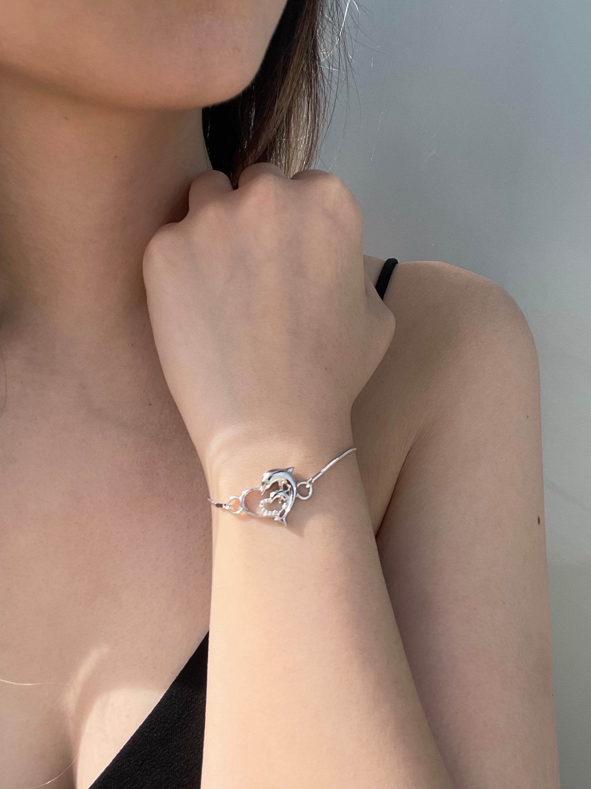 Close-up model photo showcasing a 925 sterling silver bolo bracelet on a wrist, featuring a central open heart focal piece intertwined with detailed dolphins and 0.05 Cttw Canadian diamonds.