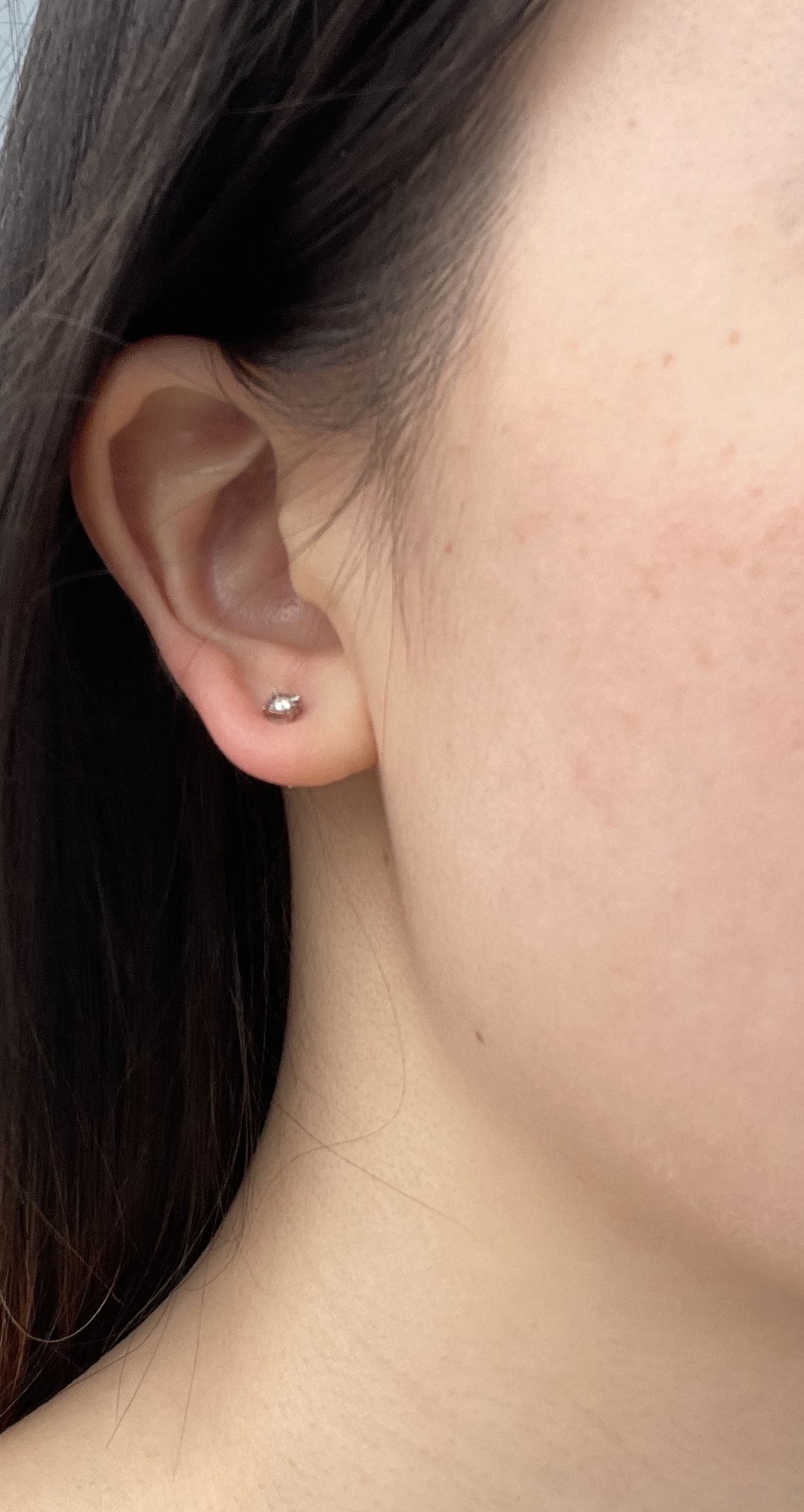 Angled side view of a 925 sterling silver solitaire stud earring on a model's earlobe, showcasing the profile, depth, and structural design of the 0.06 Cttw miracle-set Canadian diamond setting.