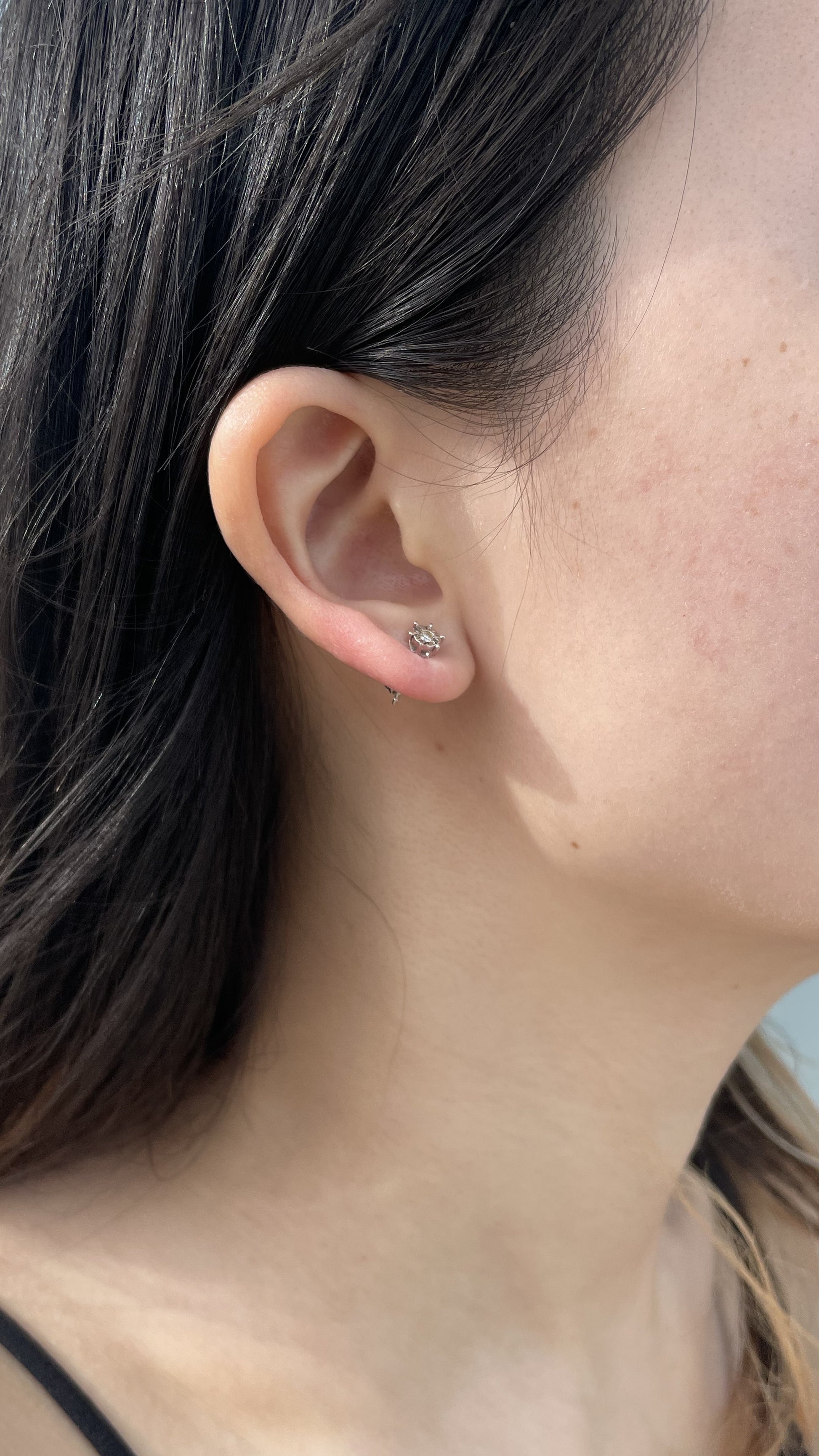 Close-up model photo showcasing a 925 sterling silver solitaire stud earring on an earlobe, highlighting the classic 6-prong miracle setting and the delicate scale of the 0.05 carat Canadian diamond center stone.