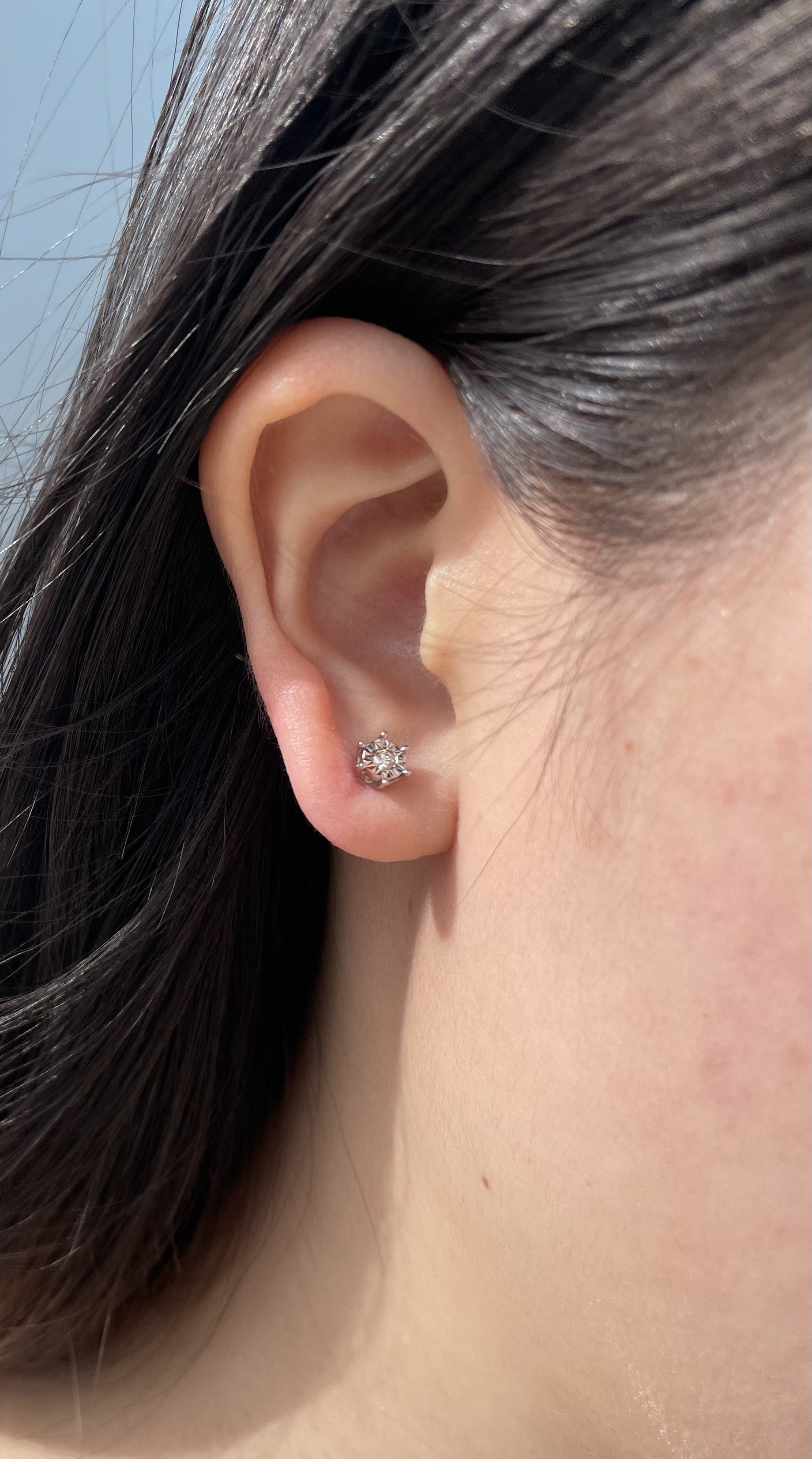 Close-up model photo showcasing a 925 sterling silver solitaire stud earring on an earlobe, highlighting the classic 6-prong miracle setting and the delicate scale of the 0.05 carat Canadian diamond center stone.