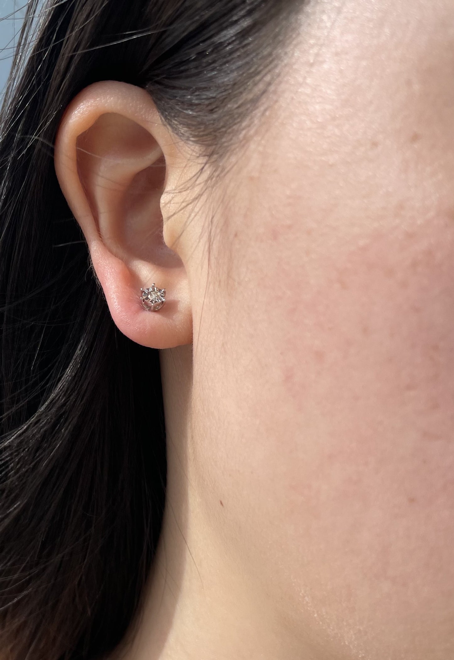 Close-up model photo showcasing a 925 sterling silver solitaire stud earring on an earlobe, highlighting the classic 6-prong miracle setting and the delicate scale of the 0.05 carat round brilliant cut Canadian diamond center stone.