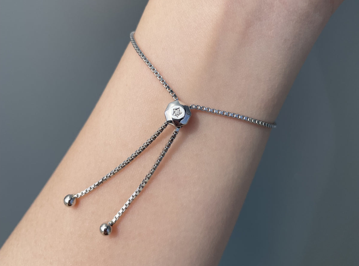 A 925 sterling silver adjustable chain bracelet with a central hexagonal bead and dangling ball charms, shown worn on a person's wrist against a soft gray background.