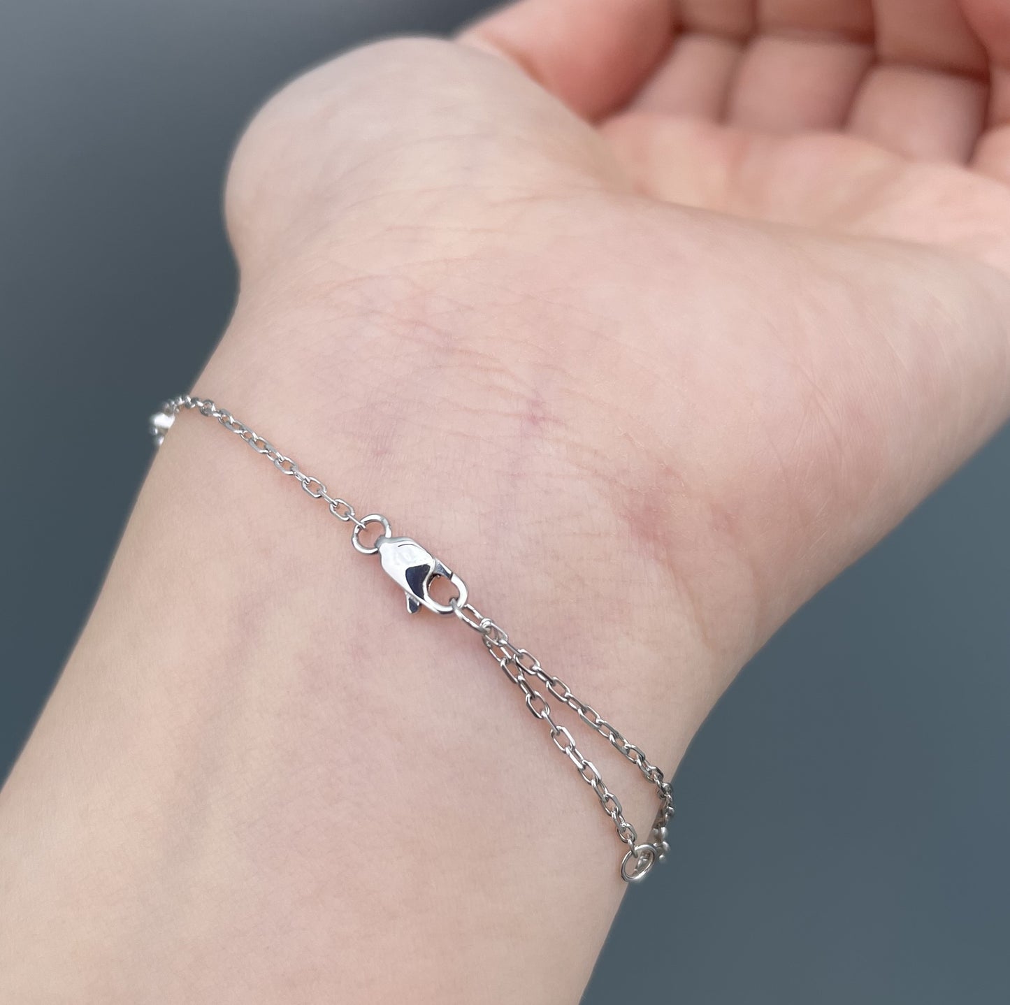 A delicate 10K white gold chain bracelet with a lobster clasp, shown worn on a person's wrist against a dark gray background.