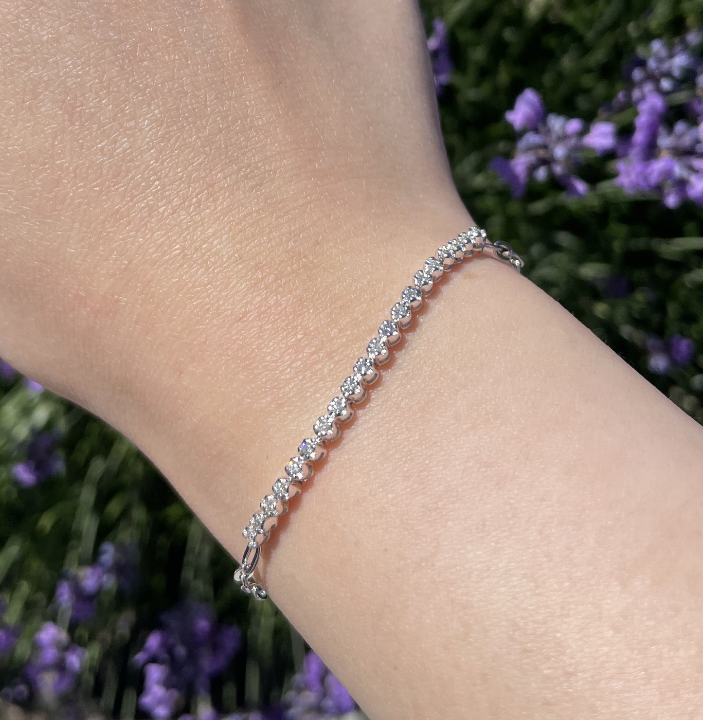 Silver and Canadian diamond bracelet on a wrist with a blurred background of purple flowers