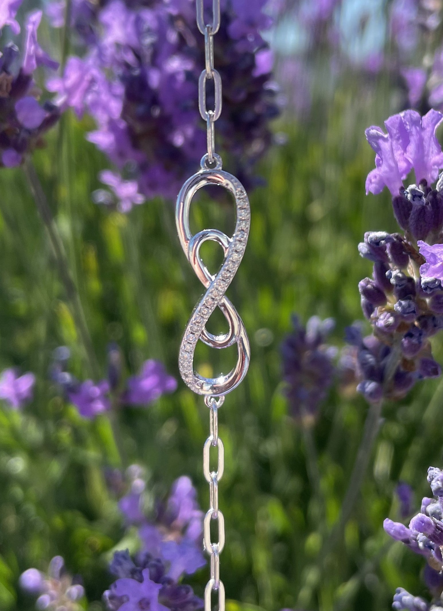 925 Sterling Silver 0.15 Ctw Natural Canadian Diamond and Infinity Symbol Chain Paperclip Bracelet against a background of lavender flowers
