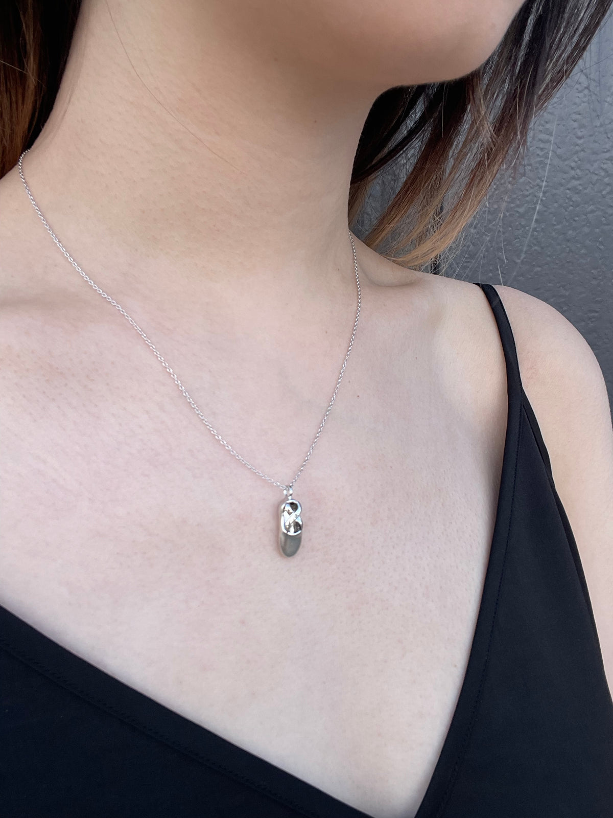 Model wearing a high-polish sterling silver ballet slipper pendant necklace, featuring an intricate cut-out design and a delicate cable chain against a black top.