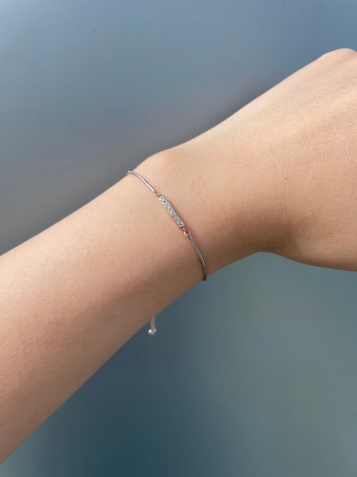 Close-up product view of a 925 sterling silver and 10K yellow gold bar adjustable bolo bracelet worn on a wrist against a grey background, showcasing the slim two-tone chain and a horizontal bar set with round brilliant cut Canadian diamonds totaling 0.10 Cttw.