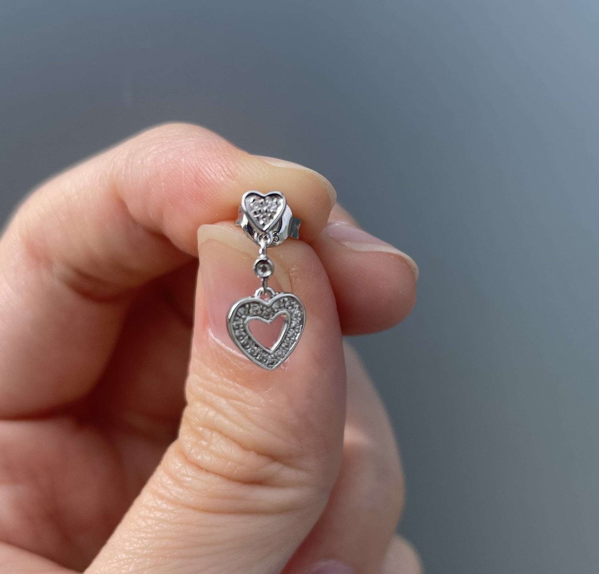 Close-up  photo showcasing a 925 sterling silver dangle earring on an earlobe, highlighting the small post stud that drops into an open heart charm paved with 0.10 Cttw Canadian diamonds.