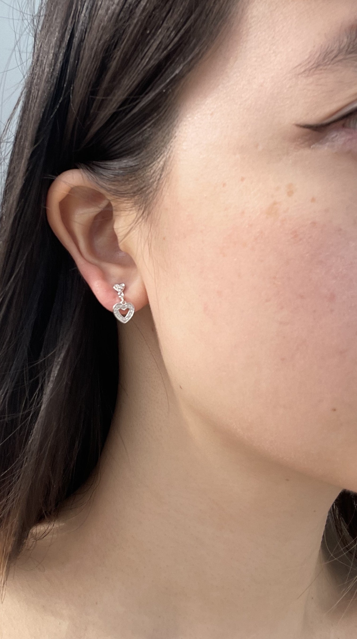Close-up model photo showcasing a 925 sterling silver dangle earring on an earlobe, highlighting the small post stud that drops into an open heart charm paved with 0.10 Cttw Canadian diamonds.