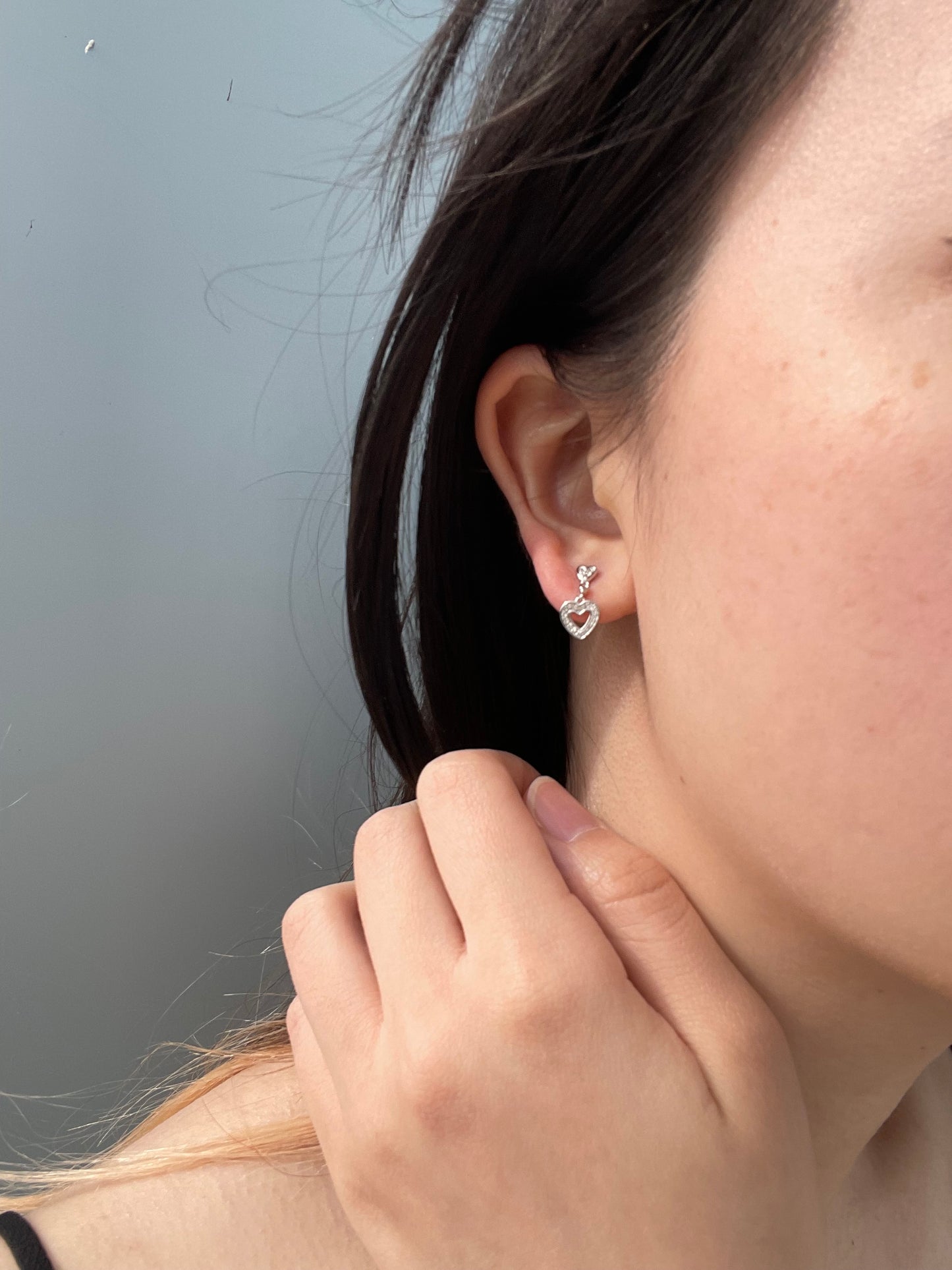 Close-up model photo showcasing a 925 sterling silver dangle earring on an earlobe, highlighting the small post stud that drops into an open heart charm paved with 0.10 Cttw Canadian diamonds.