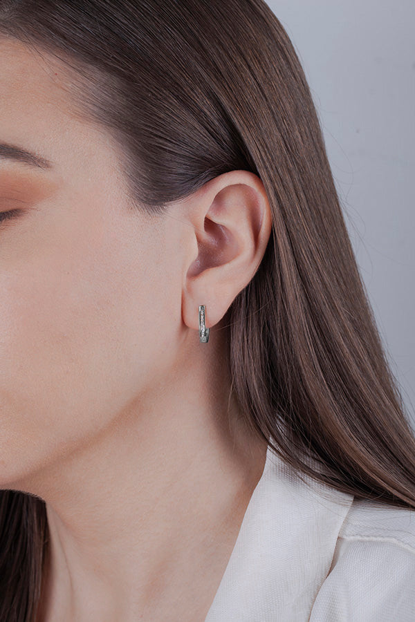 Close-up of a person wearing 10k white gold hoop diamond earring with a neutral background
