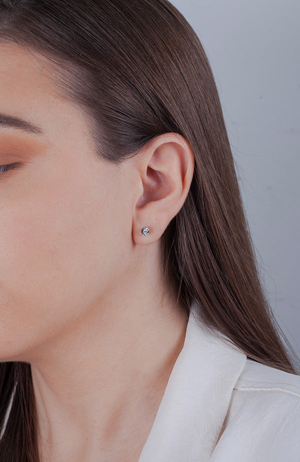 Close-up of a person wearing a solitaire diamond miracle-setting stud earring against a neutral background