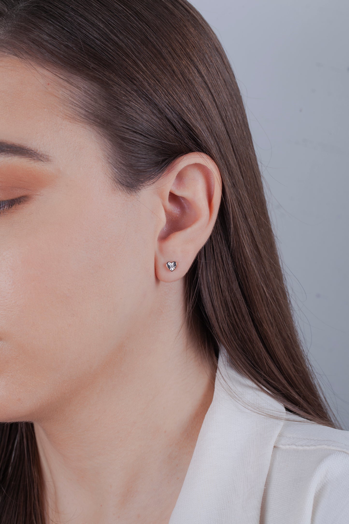 Close-up of a person wearing a diamond heart shaped earring with a neutral background