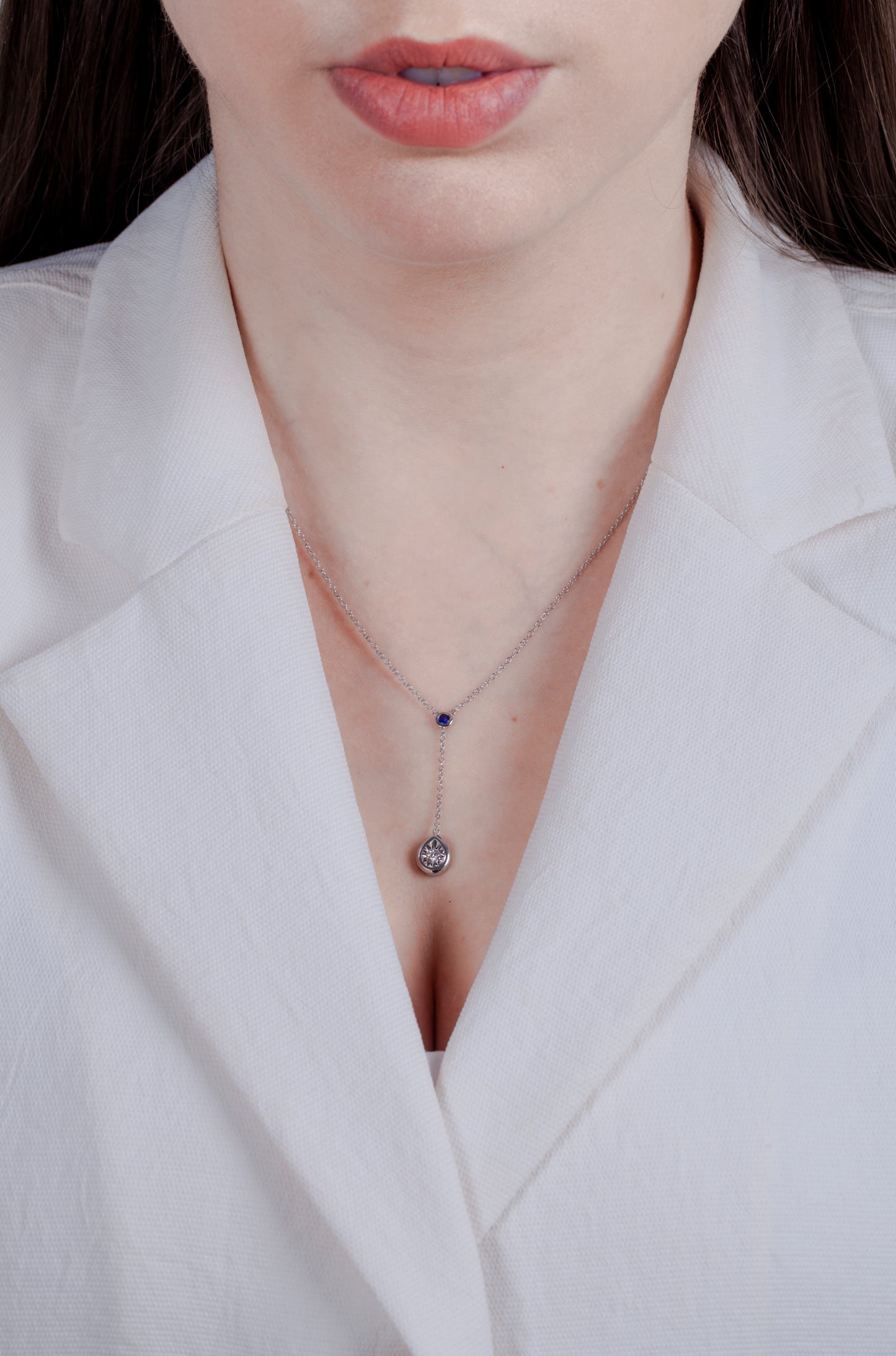 Person wearing a white blazer with dangle necklace featuring round  sapphire and teardrop shape design miracle setting diamond