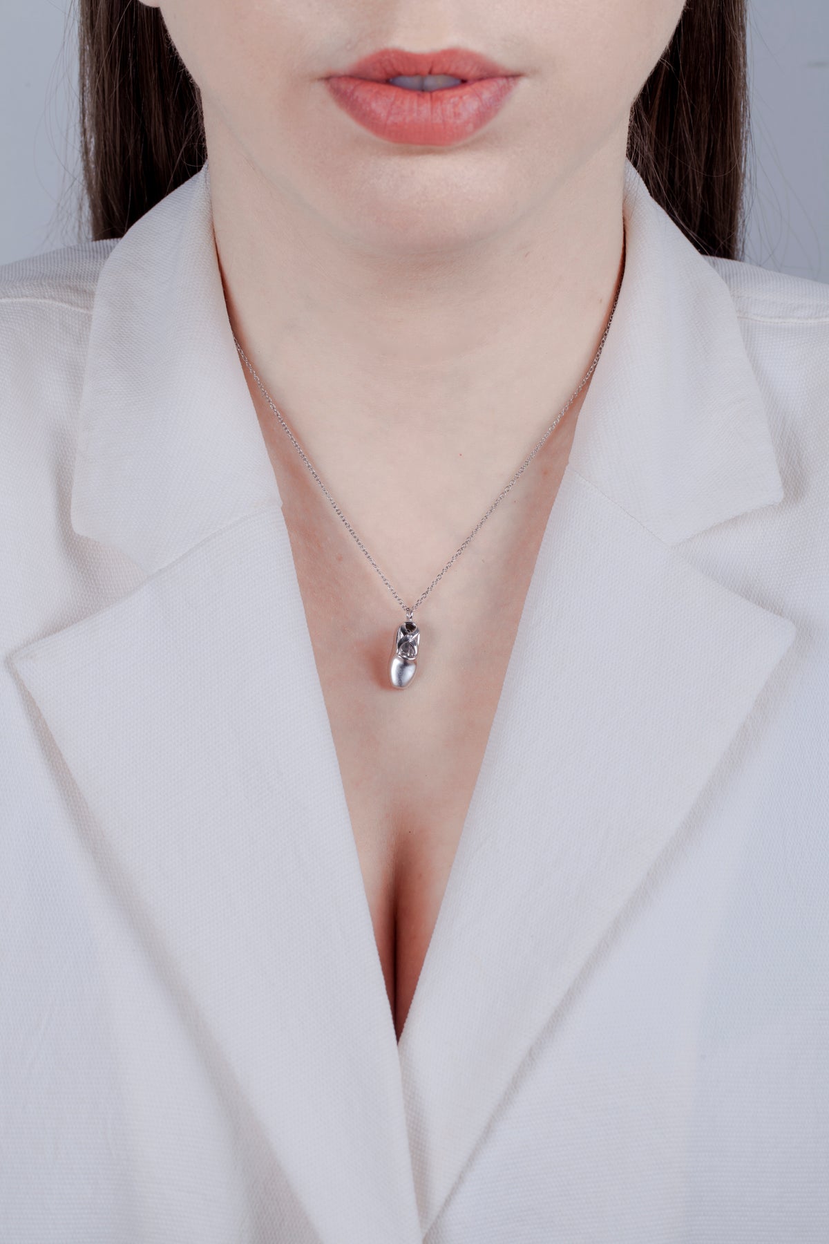 Model wearing a high-polish sterling silver ballet slipper pendant necklace, featuring an intricate cut-out design and a delicate cable chain against a cream-colored blazer.
