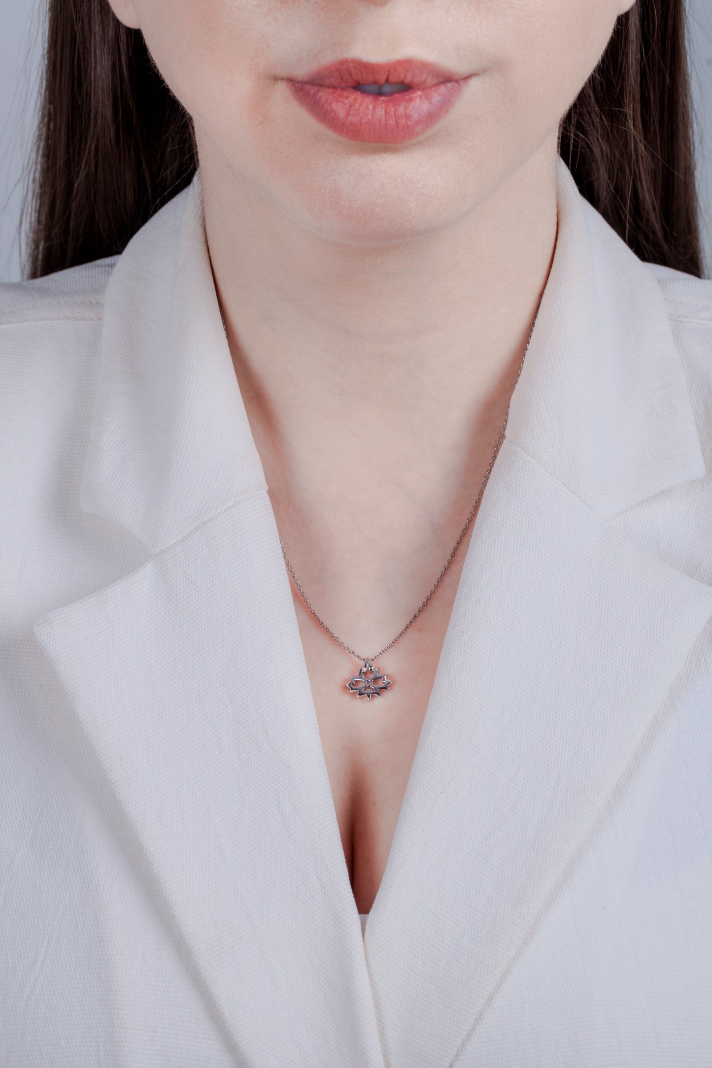 Sterling silver maple leaf pendant with a 0.06 carat Canadian diamond and a high-polish finish, shown on a model in a white blazer. The image highlights the shiny, reflective surface and the 18-inch rolo chain's fit, offering a clean and professional look.