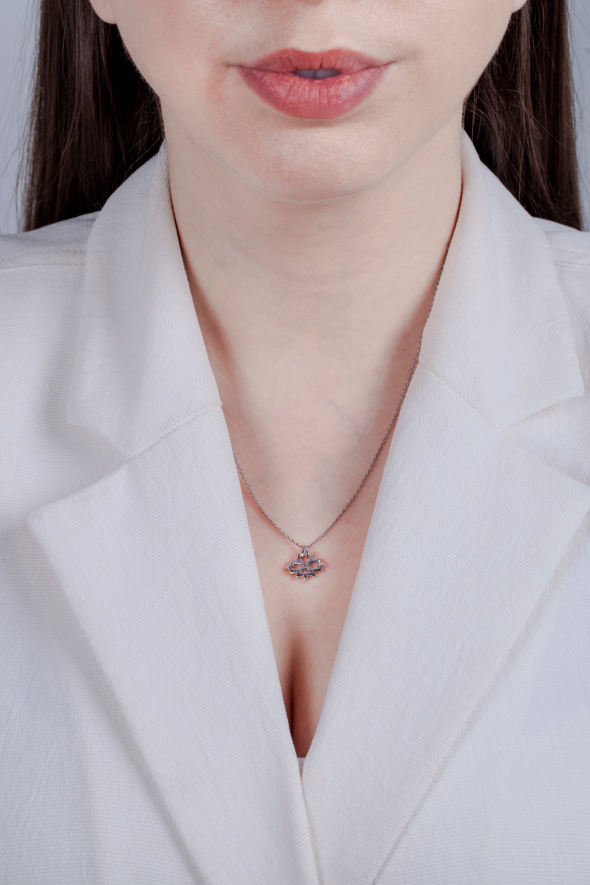 Sterling silver maple leaf pendant with a 0.06 carat Canadian diamond and a high-polish finish, shown on a model in a white blazer. The image highlights the shiny, reflective surface and the 18-inch rolo chain's fit, offering a clean and professional look.