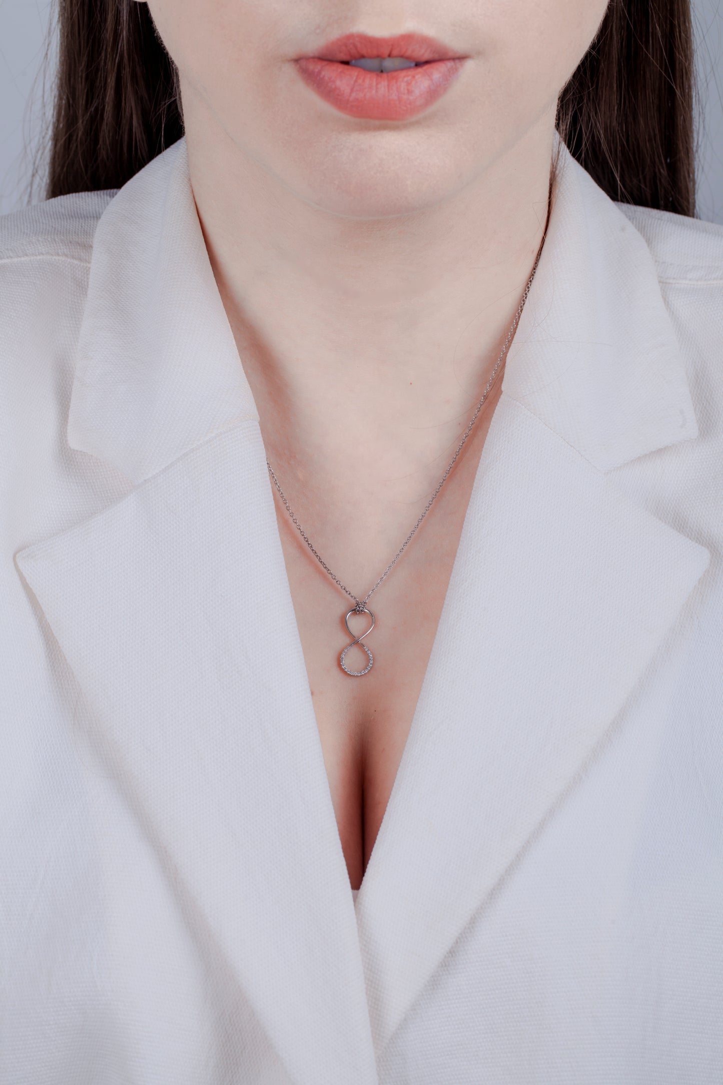 Model in a white blazer wearing a 925 sterling silver Canadian diamond vertical infinity pendant. The thin design and rolo chain provide a minimalistic look.