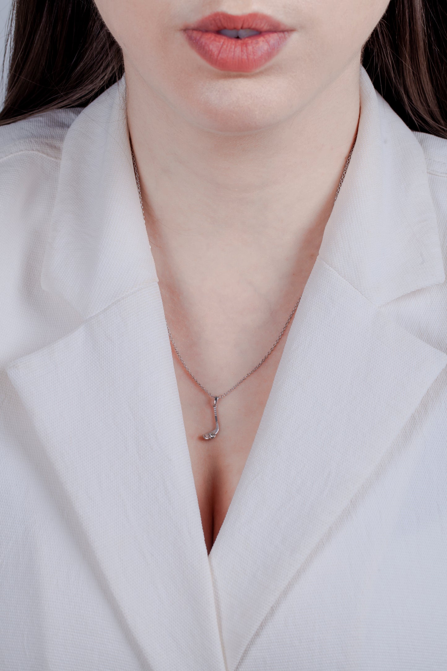 Model in a white blazer wearing a matte finish solid 925 sterling silver hockey stick pendant. A 0.05 carat Canadian diamond is set at the base of the blade, designed to look like a hockey puck. This matte, minimalistic charm hangs from an 18-inch rolo chain.
