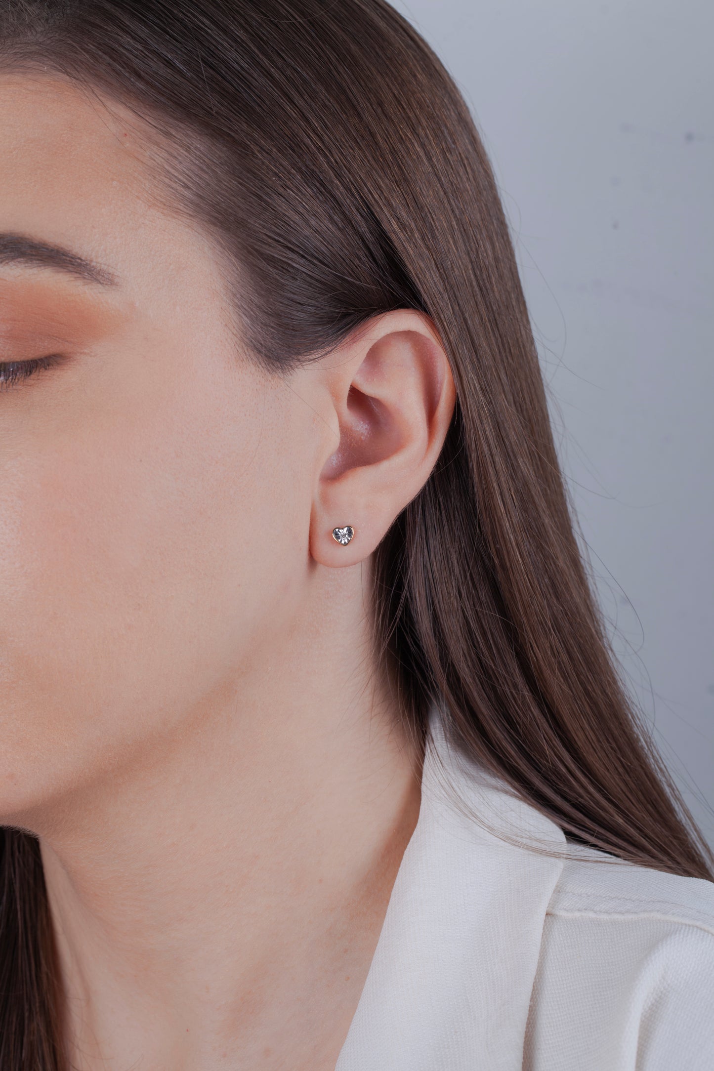 Close-up of a person wearing a 10k yellow gold heart diamond stud earring against a neutral background