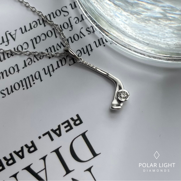 Close up of 925 Sterling Silver hockey pendant with a 0.05 carat Canadian diamond on a book page, featuring 'Polar Light Diamonds' branding.