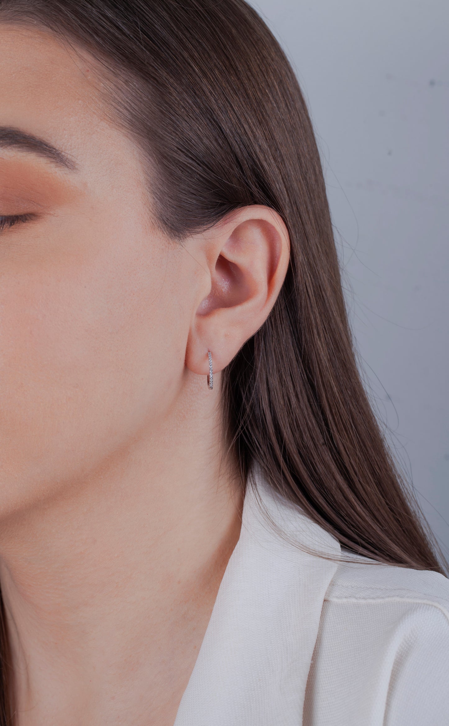Minimalist jewelry styling: A model wearing Canadian diamond sterling silver huggies and a white blazer. Close-up portrait focusing on the elegant sparkle of the diamond hoop earrings.