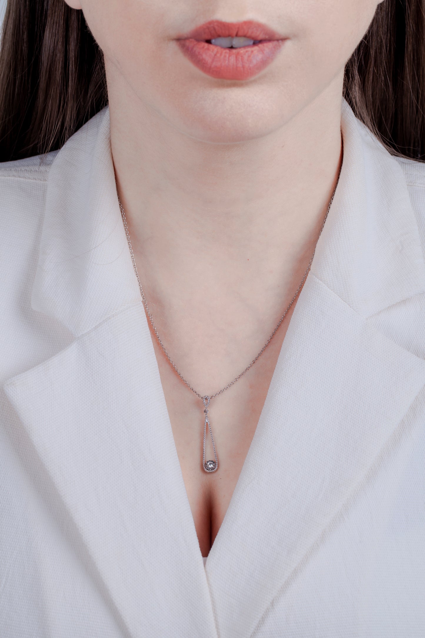 Close-up of a model wearing a milgrain detail silver teardrop themed necklace and a solitaire miracle setting diamond with a white blazer