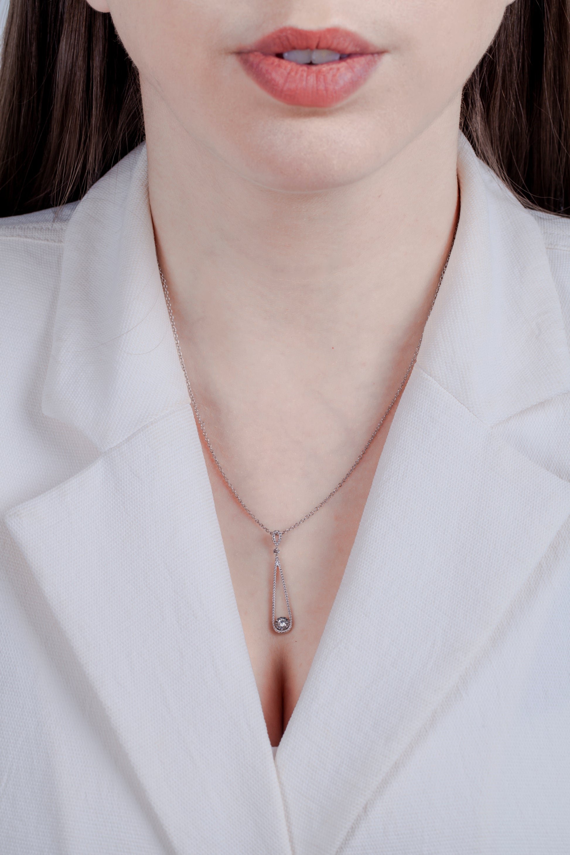 Close-up of a model wearing a milgrain detail silver teardrop themed necklace and a solitaire miracle setting diamond with a white blazer