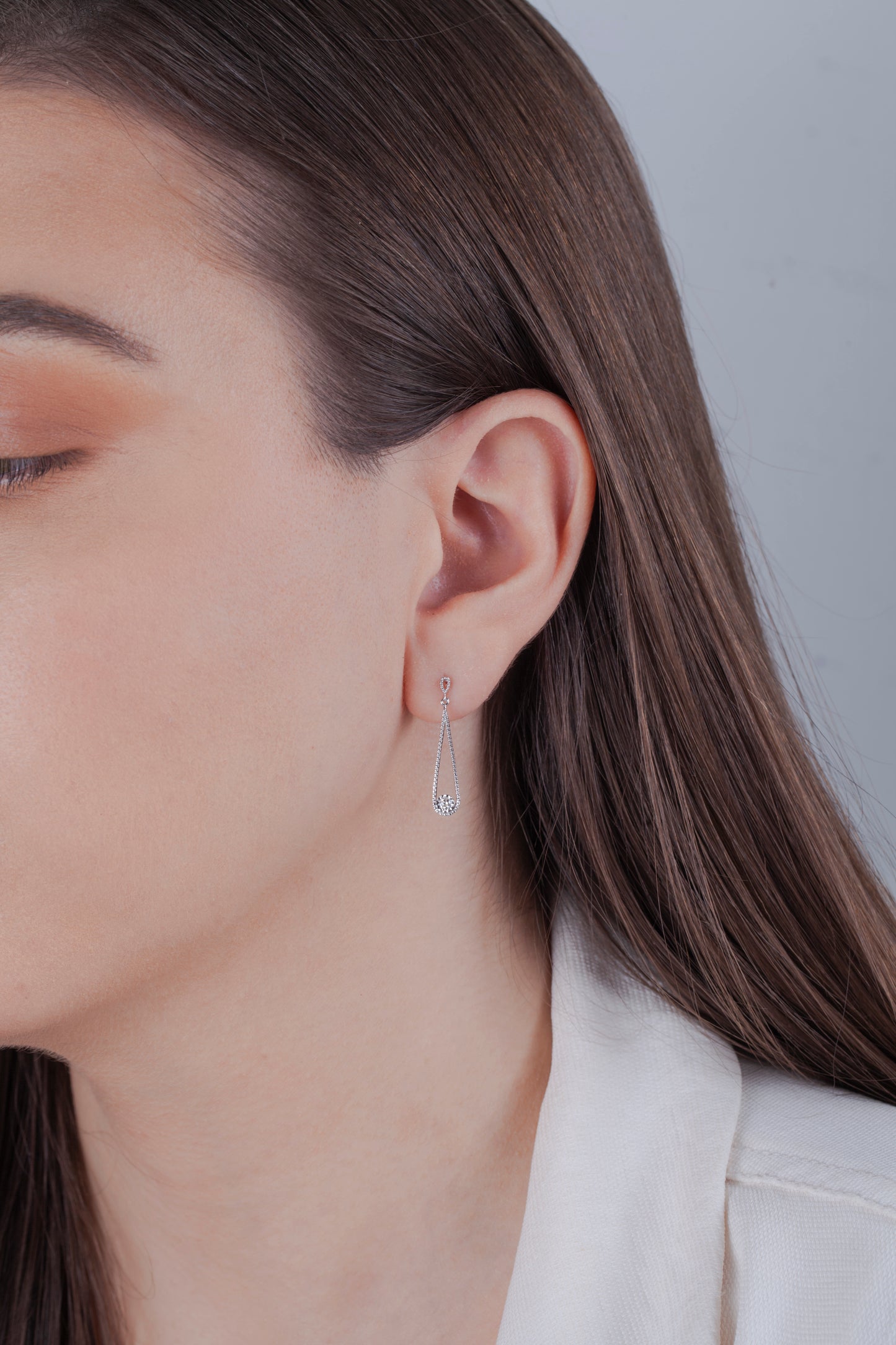 Close-up of a person wearing a silver teardrop style earring with miracle setting Canadian diamond with a blurred background