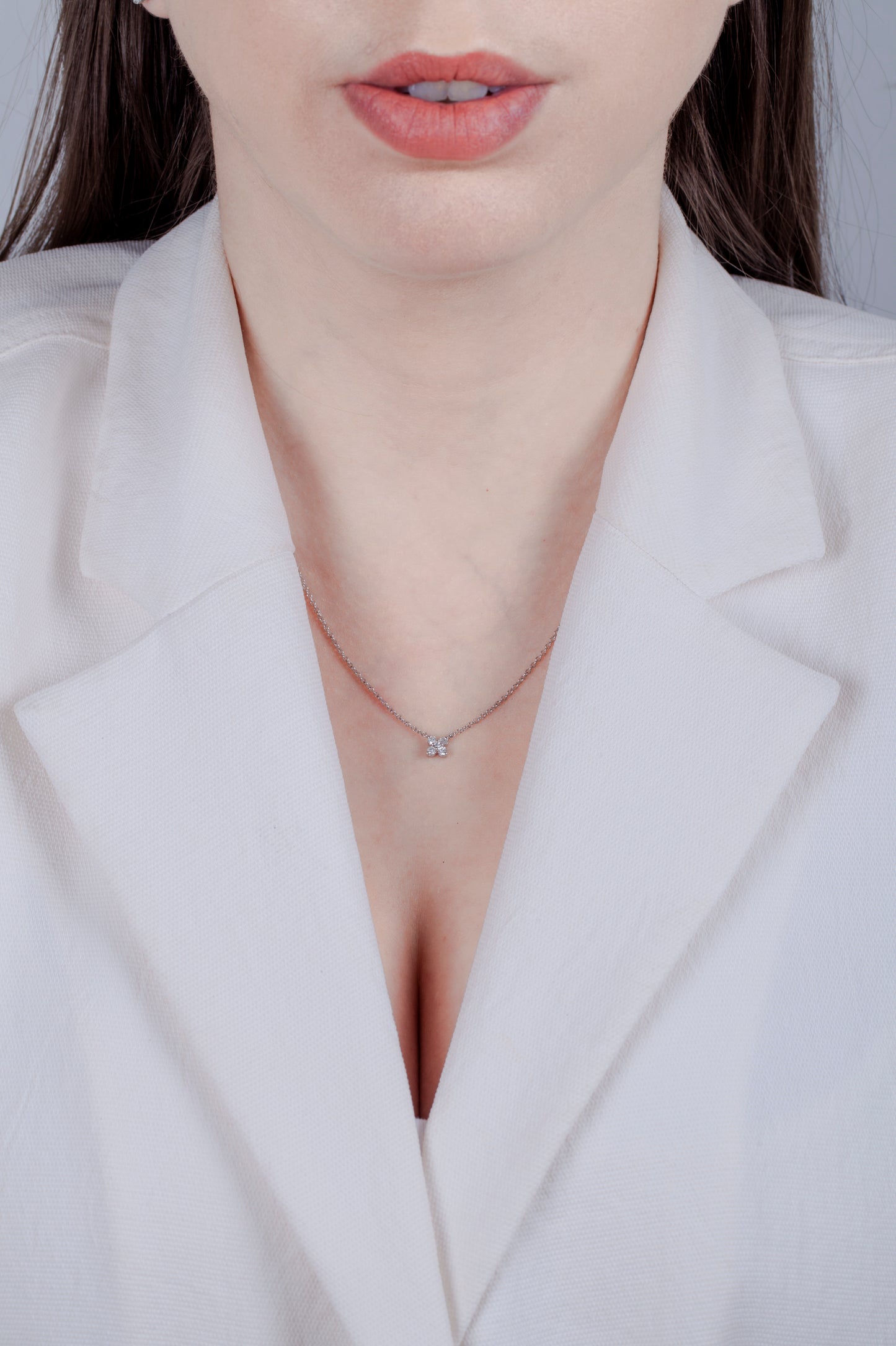 Person wearing a white blazer with a necklace featuring a floral inspired diamond pendant.