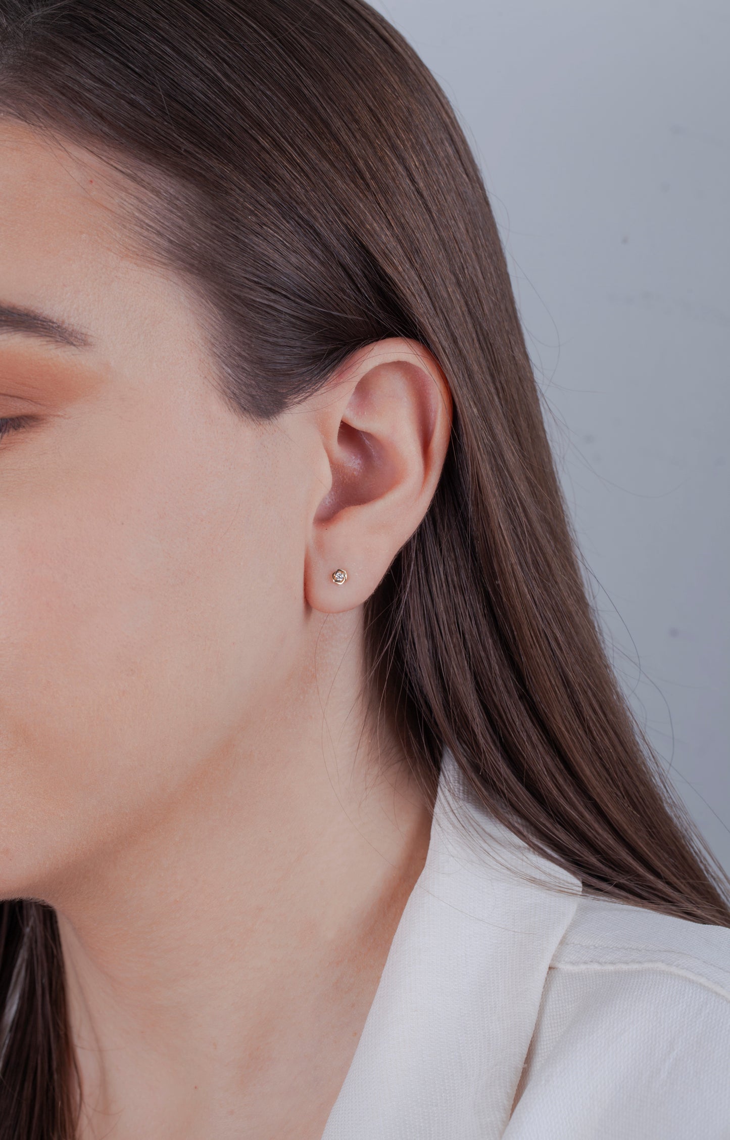 Close-up of a person wearing a dainty 10k yellow gold solitaire rose design Canadian diamond earring with a plain background