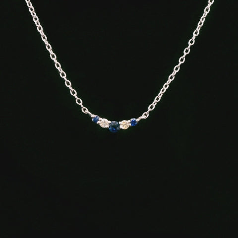 A 925 sterling silver wave-shaped pendant rotating to show its curved design. The pendant is set with three blue sapphires and two Canadian diamonds that catch the light.