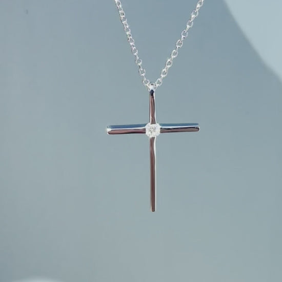 Product showcase video for the .925 Sterling Silver 1/8 Cttw Canadian Certified Diamond Solitaire Thin Cross Pendant Necklace. Includes close-up views of the delicate cross pendant set with a natural solitaire Canadian diamond (H-I color, SI2-I1 clarity), along with an on-model view demonstrating the 16"-18" chain fit and scale.