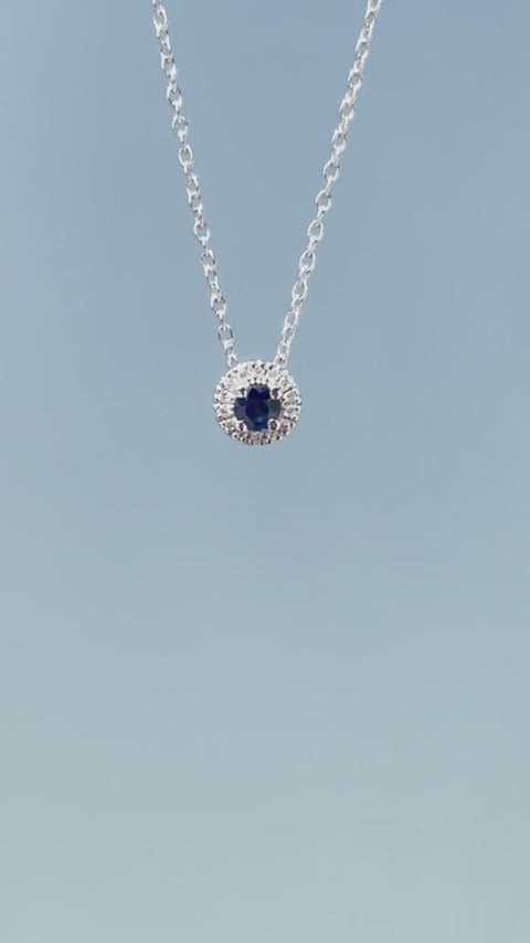 Product showcase video for the .925 Sterling Silver 1/10 Cttw White Diamond & Blue Sapphire 1/4" Halo Pendant Necklace. Includes close-up details of the central sapphire surrounded by a sparkling diamond halo (H-I color, SI2-I1 clarity) and an on-model view demonstrating the 16"-18" chain length.