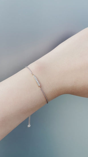 Short product video showcasing the 925 sterling silver and 10K yellow gold bolo bracelet, panning from a close-up of the 0.10 Cttw Canadian diamond bar setting to a demo of the model adjusting the bolo chain on her wrist to showcase the adjustable element.