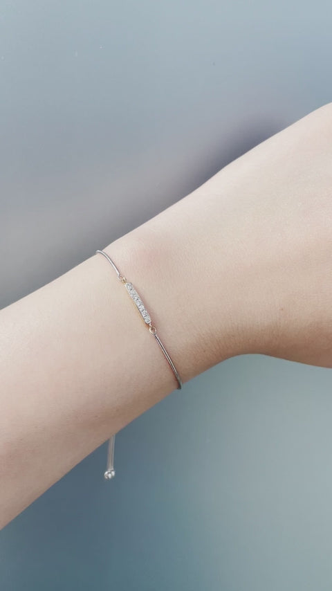 Short product video showcasing the 925 sterling silver and 10K yellow gold bolo bracelet, panning from a close-up of the 0.10 Cttw Canadian diamond bar setting to a demo of the model adjusting the bolo chain on her wrist to showcase the adjustable element.