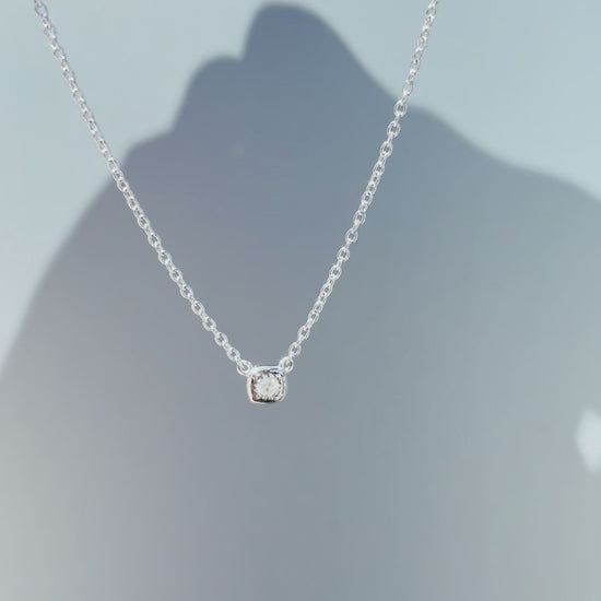 Product showcase video for the Sterling Silver 0.04 Cttw Canadian Diamond Solitaire Cushion Shaped Miracle Plate Bezel-Set Necklace. Features close-ups of the cushion-shaped miracle plate bezel setting with a natural Canadian diamond (H-I color, SI2-I1 clarity), alongside an on-model view demonstrating chain drop and scale.