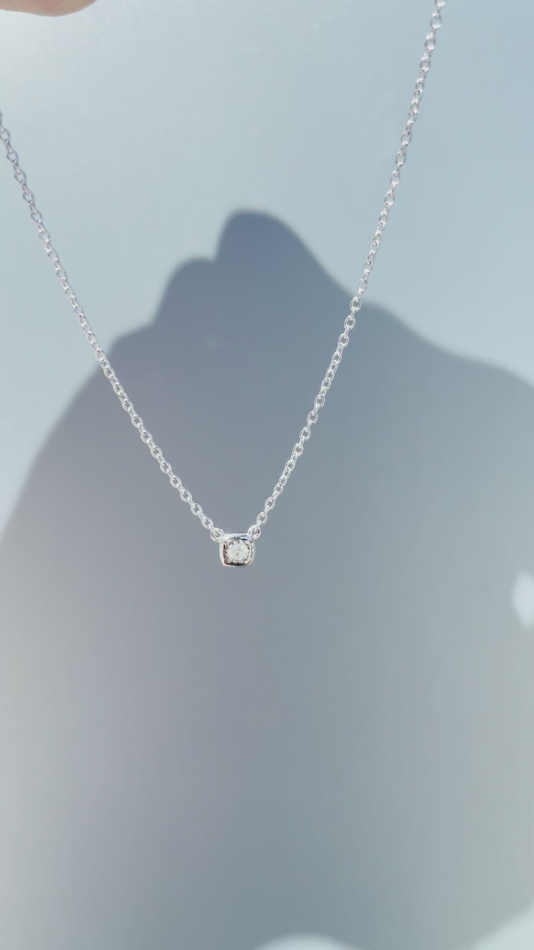 Product showcase video for the Sterling Silver 0.04 Cttw Canadian Diamond Solitaire Cushion Shaped Miracle Plate Bezel-Set Necklace. Features close-ups of the cushion-shaped miracle plate bezel setting with a natural Canadian diamond (H-I color, SI2-I1 clarity), alongside an on-model view demonstrating chain drop and scale.