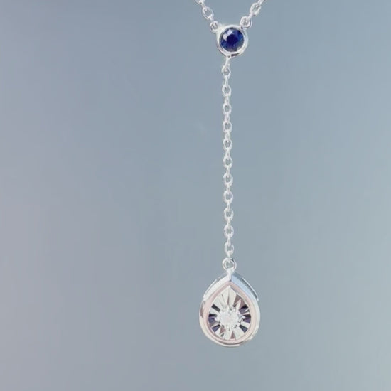 Product showcase video for the .925 Sterling Silver Blue Sapphire & White Diamond Y Style Pear Shaped Miracle Set Dangle Pendant Necklace. Features close-up details of the pear-shaped miracle setting and dangling sapphire accent (H-I color, SI2-I1 clarity), along with an on-model view showcasing the Y-drop silhouette on the 16"-18" adjustable chain.