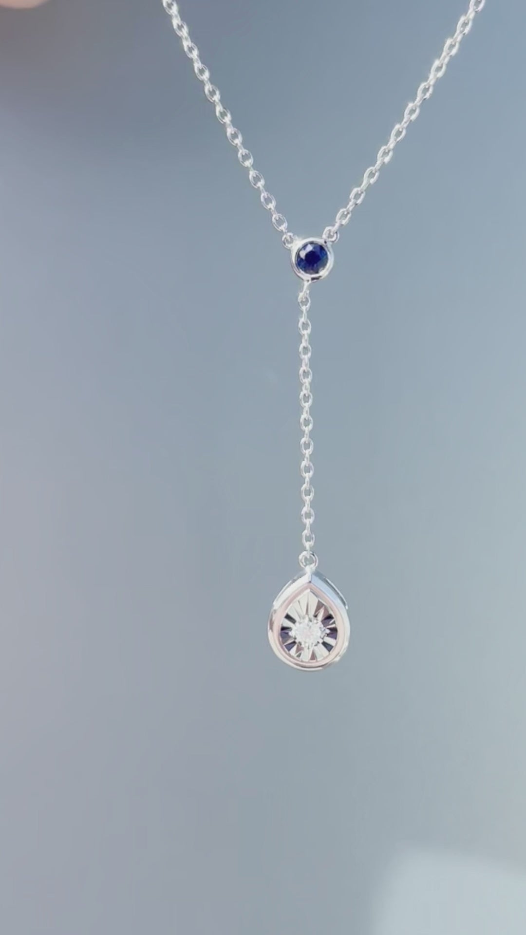 Product showcase video for the .925 Sterling Silver Blue Sapphire & White Diamond Y Style Pear Shaped Miracle Set Dangle Pendant Necklace. Features close-up details of the pear-shaped miracle setting and dangling sapphire accent (H-I color, SI2-I1 clarity), along with an on-model view showcasing the Y-drop silhouette on the 16"-18" adjustable chain.