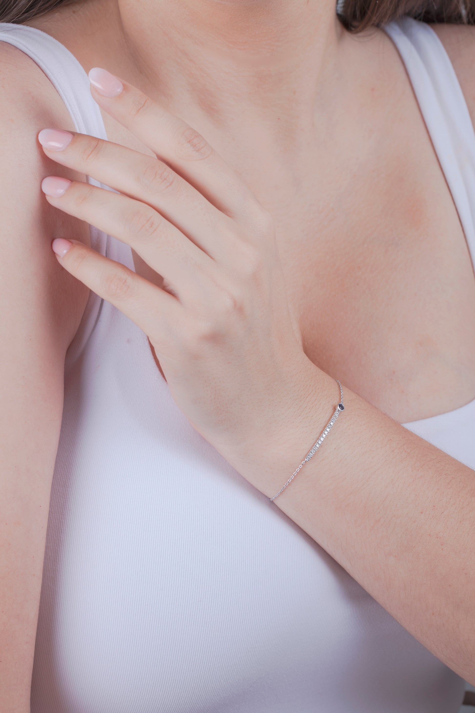 Person wearing a white tank top with a close-up of sapphire and diamond bar bracelet